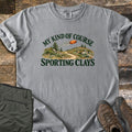 My Kind of Course Comfort Colors T-shirt in Grey, laid flat. The words My Kind of Course arch over a painted trail winding between grassy, rocky hills with pine trees as an orange clay target flies past, above Sporting Clays. Olive pants and brown hiking boots sit on weathered wood.