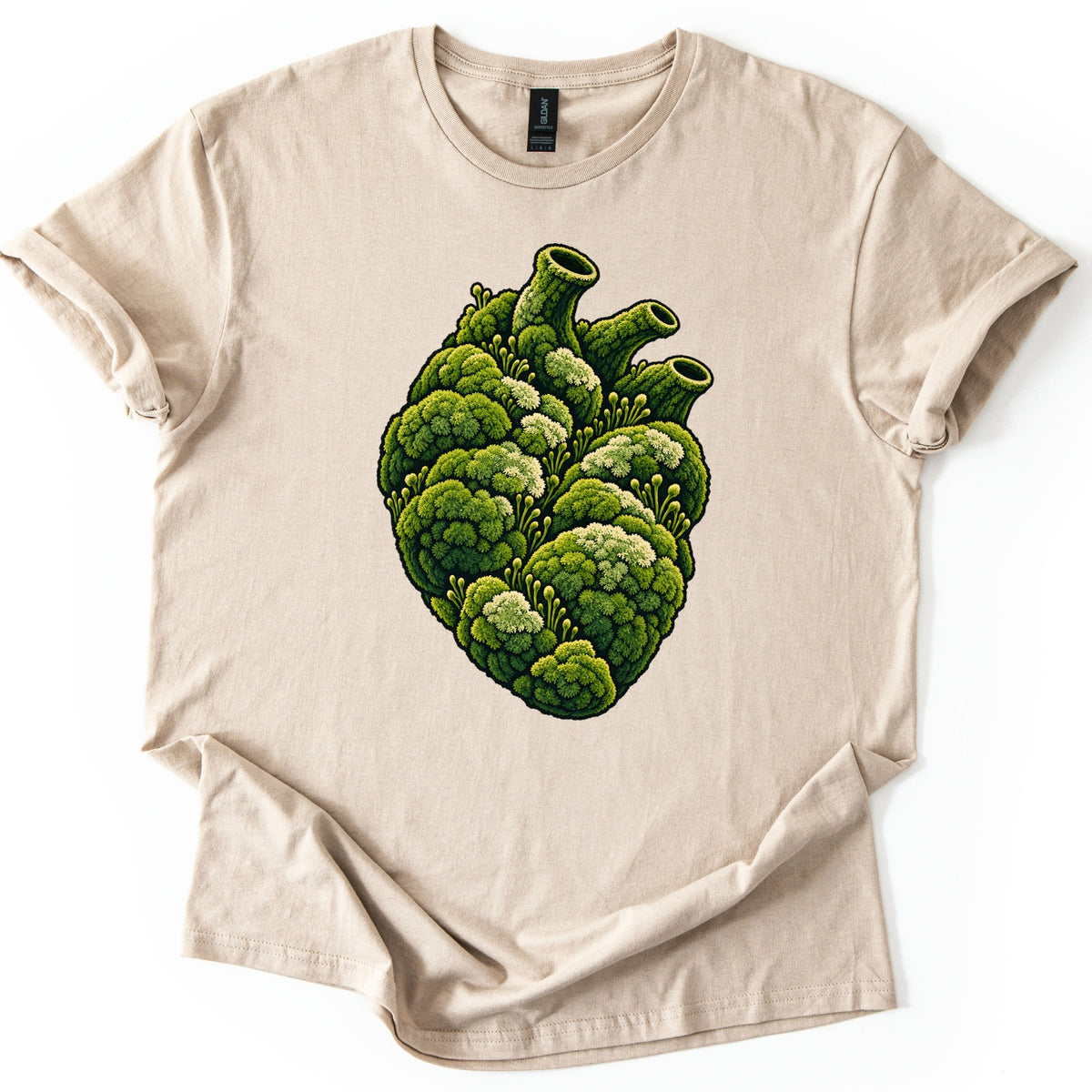 Moss Heart Comfort Colors T-shirt in Sand, laid flat. An anatomical heart made of clumps of green moss, with pale tufts, small sprouting stalks and three tube-like vessels on top, with no words. The shirt lies on a white surface with sleeves cuffed.
