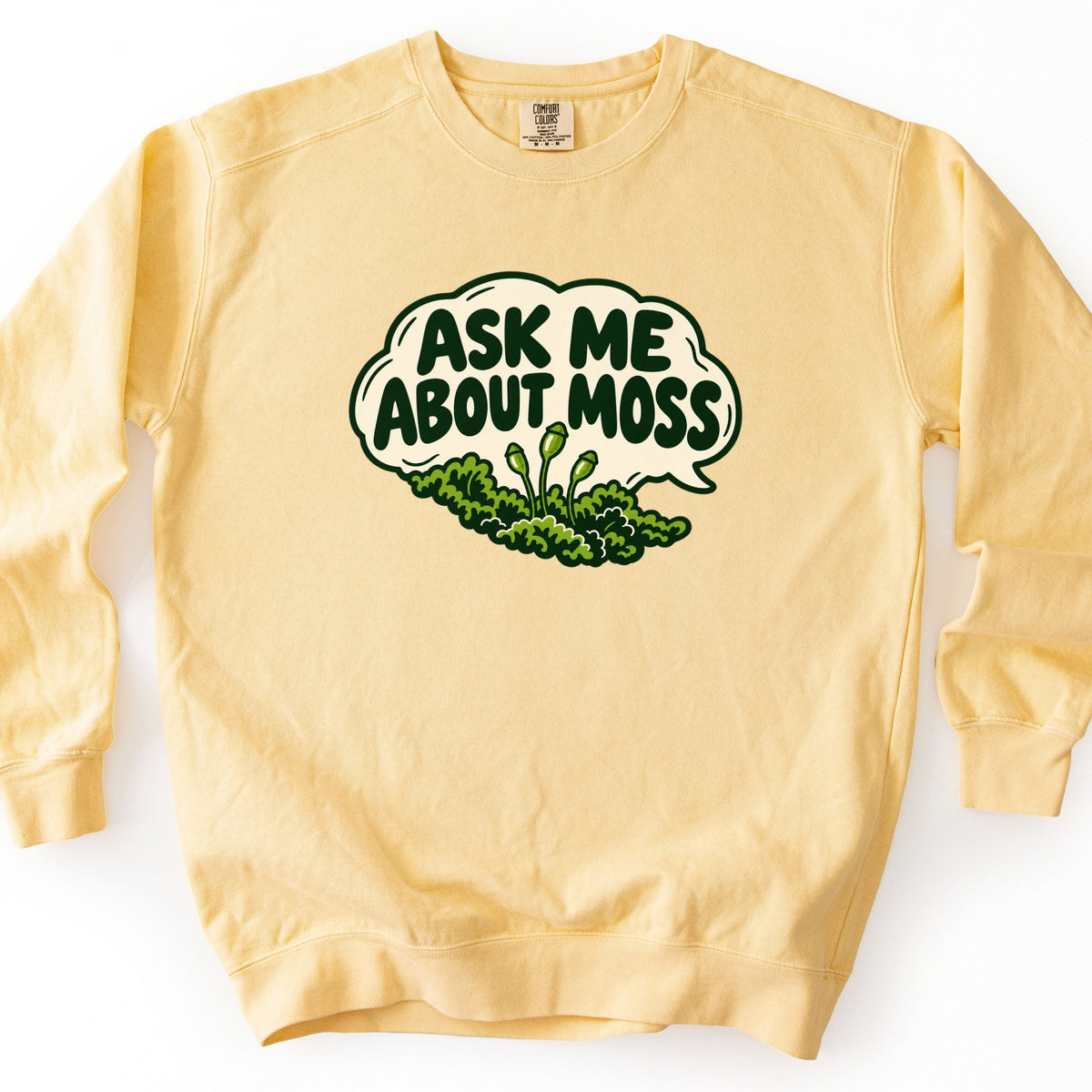 Ask Me About Moss Comfort Colors crewneck sweatshirt in Butter, laid flat. A cream speech bubble outlined in dark green holds the words Ask Me About Moss in bold green letters, above a clump of green moss with three thin stalks topped by spore capsules. Set on a white background.