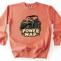 Power Nap Comfort Colors crewneck sweatshirt in Terracotta, laid flat. A cartoon bearded man in a cap naps slumped over the steering wheel of a green side-by-side UTV among pine trees and mud, above the words Power Nap in cream letters. Shown on a white background.