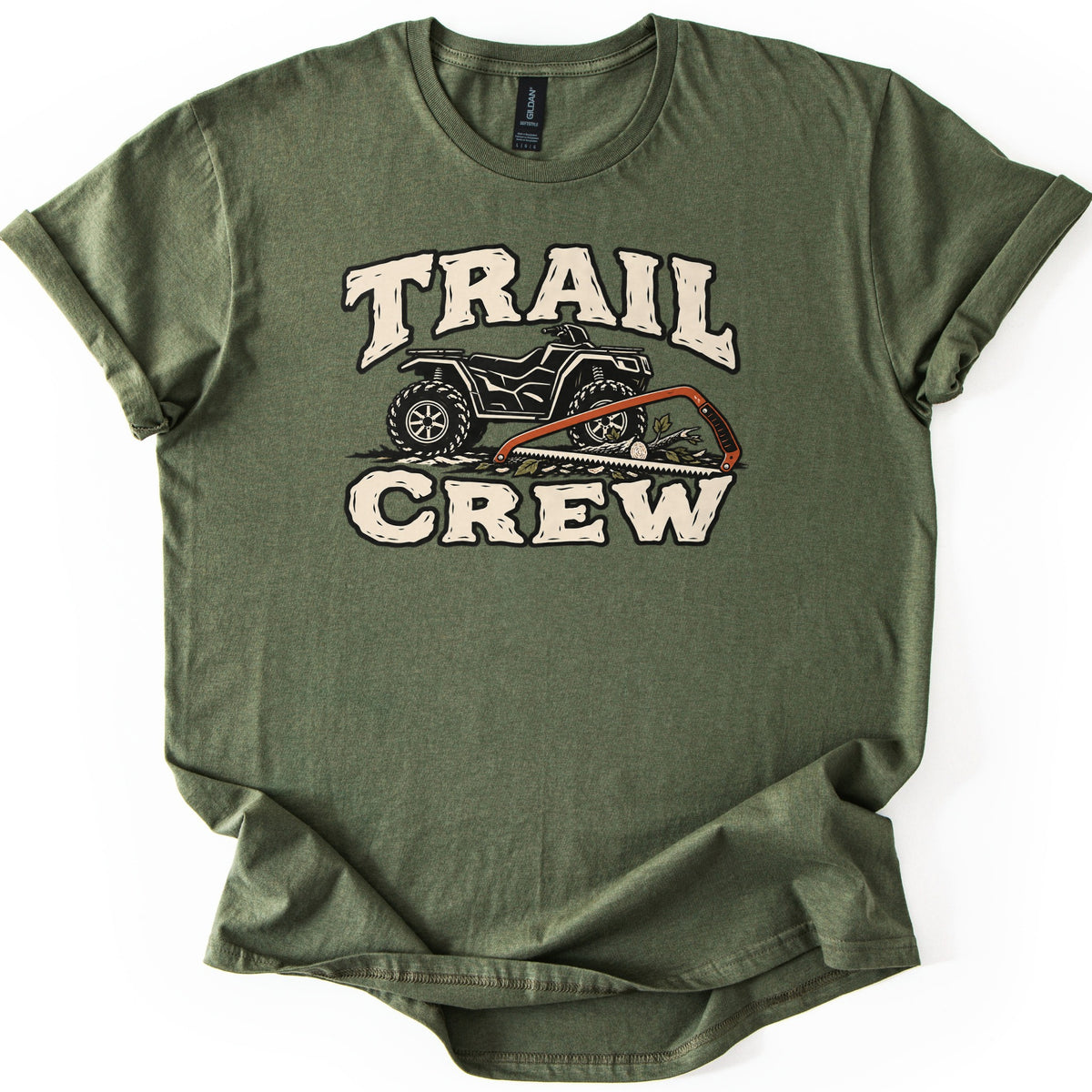 Trail Crew Comfort Colors T-shirt in Military Green, laid flat. Cream distressed letters read TRAIL above and CREW below a black ATV, with an orange bow saw resting on a cut branch and leaves in front of it. The shirt has rolled sleeves on a white background.