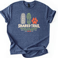 Shared Trail Room for Every Footprint Comfort Colors T-shirt in Heather Navy, laid flat. A cream bike tire tread, a green boot sole print and an orange paw print sit above the words Shared Trail, Room for Every Footprint, MTB. The sleeves are cuffed, on a plain white background.