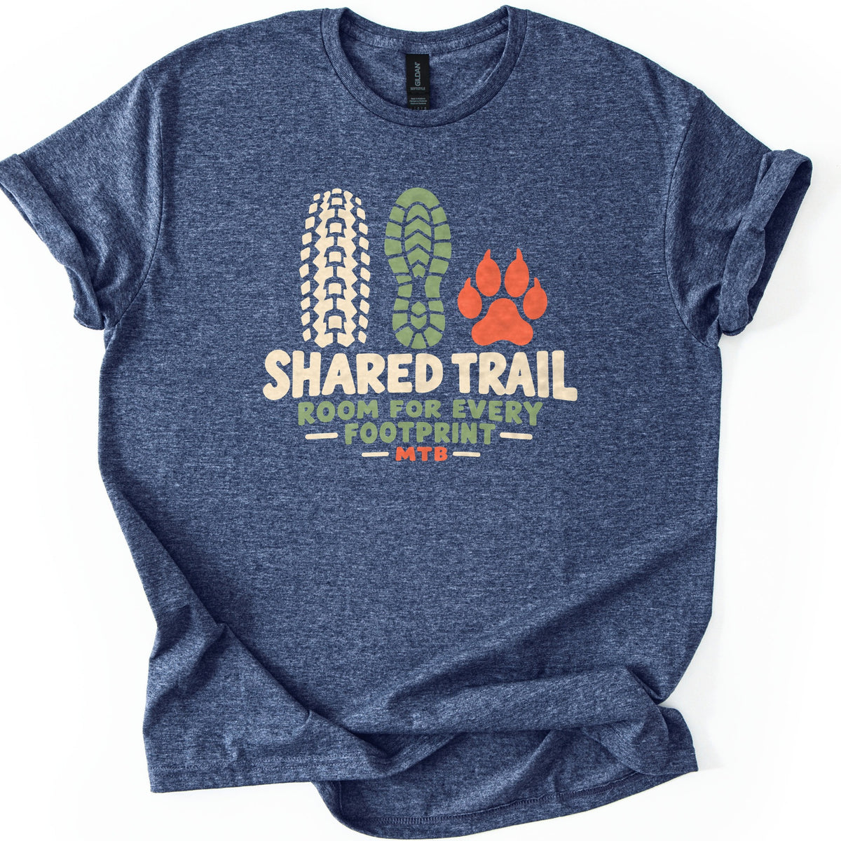 Shared Trail Room for Every Footprint Comfort Colors T-shirt in Heather Navy, laid flat. A cream bike tire tread, a green boot sole print and an orange paw print sit above the words Shared Trail, Room for Every Footprint, MTB. The sleeves are cuffed, on a plain white background.