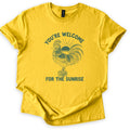 You're Welcome For The Sunrise Comfort Colors T-shirt in Daisy, laid flat. Dark green line art of a crowing rooster standing on a wooden post in front of a rising sun, with the words You're Welcome arched above and For The Sunrise below. Sleeves are rolled on a white background.