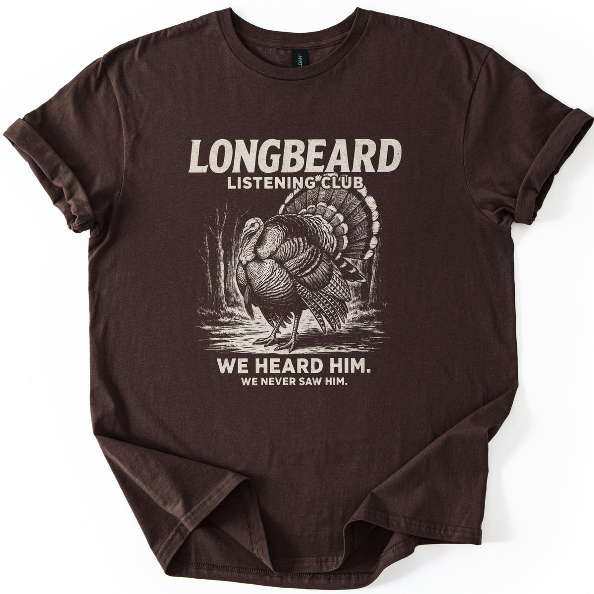 Longbeard Listening Club Comfort Colors T-shirt in Dark Chocolate, laid flat. A cream engraving-style wild turkey in full strut stands in a wooded clearing under LONGBEARD LISTENING CLUB, with WE HEARD HIM. WE NEVER SAW HIM. below. The sleeves are cuffed on a white background.