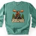 Wide Load Narrow Trail Comfort Colors crewneck sweatshirt in Light Green, laid flat. A cartoon moose with big antlers, a helmet and goggles rides a green ATV over a dirt trail between pine trees, above the words Wide Load Narrow Trail. Shown on a white background.