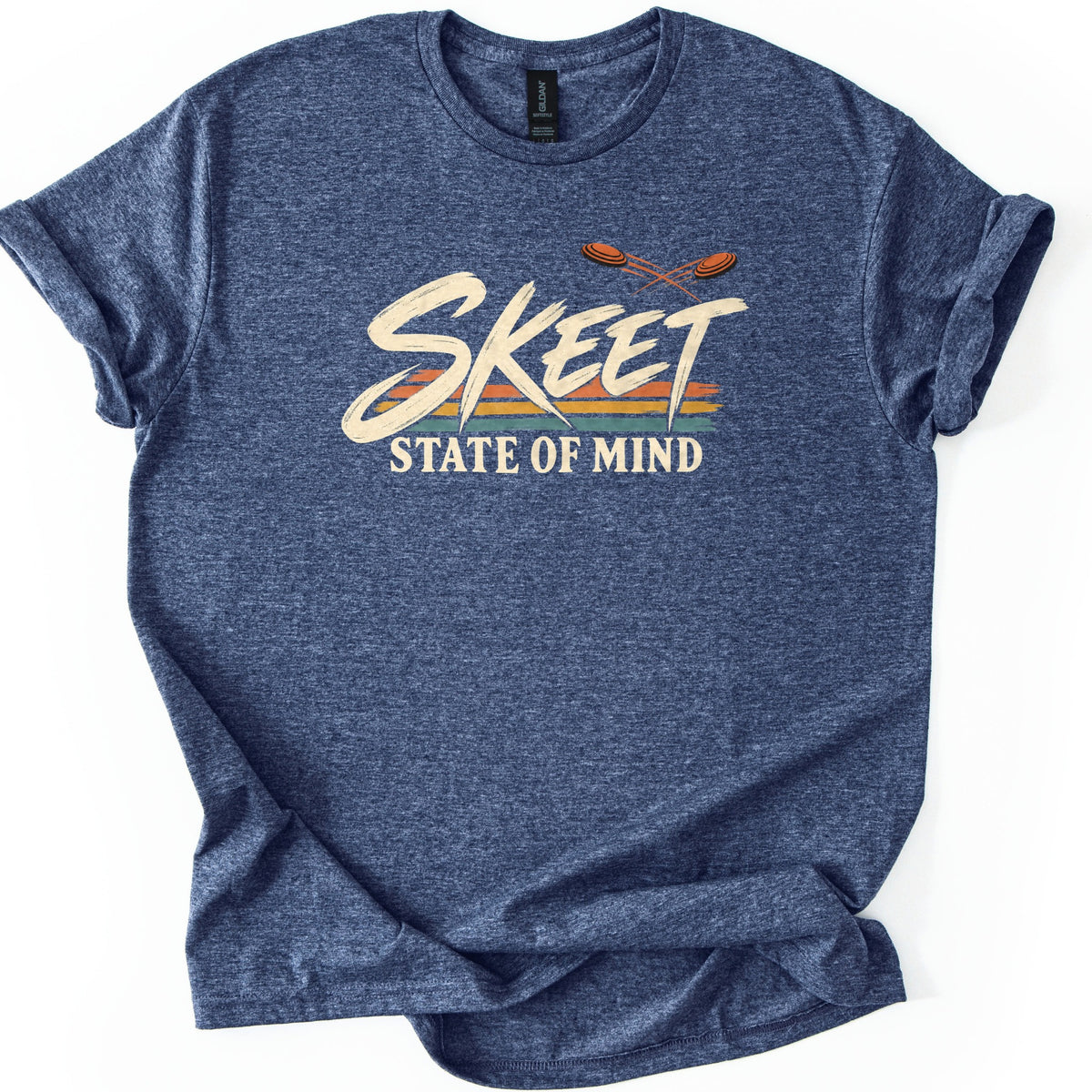 Skeet State of Mind Comfort Colors T-shirt in Heather Navy, laid flat. The word SKEET in cream brushstroke letters over orange, gold and teal stripes, with two orange clay targets flying above and STATE OF MIND below. Sleeves are cuffed on a white background.