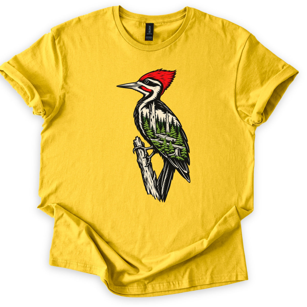 Woodpecker Forest Comfort Colors T-shirt in Daisy, laid flat. A red-crested woodpecker perches on a broken branch, its black and cream body filled with a green pine forest scene. No words are printed. The sleeves are cuffed and the shirt lies on a white background.
