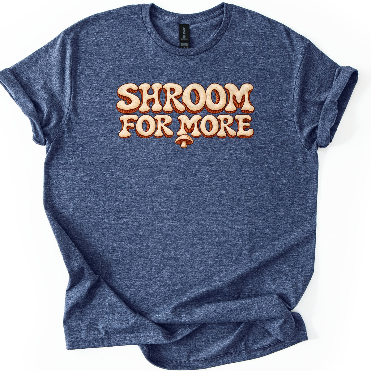 Shroom for More Comfort Colors T-shirt in Heather Navy, laid flat. Cream bubble letters with a rust-orange 3D outline read Shroom For More, with a small mushroom hanging below the M. The sleeves are rolled and the shirt lies on a white background.