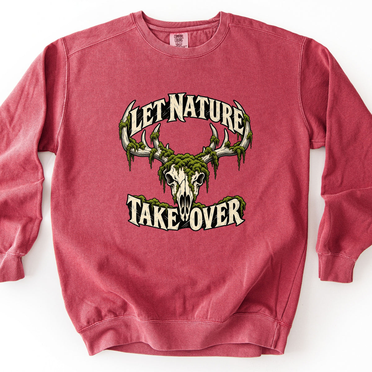 Let Nature Take Over Comfort Colors crewneck sweatshirt in Crimson, laid flat. A bleached deer skull with antlers draped in green moss sits between the words Let Nature arched above and Take Over below, in cream lettering. Shown on a plain white background.