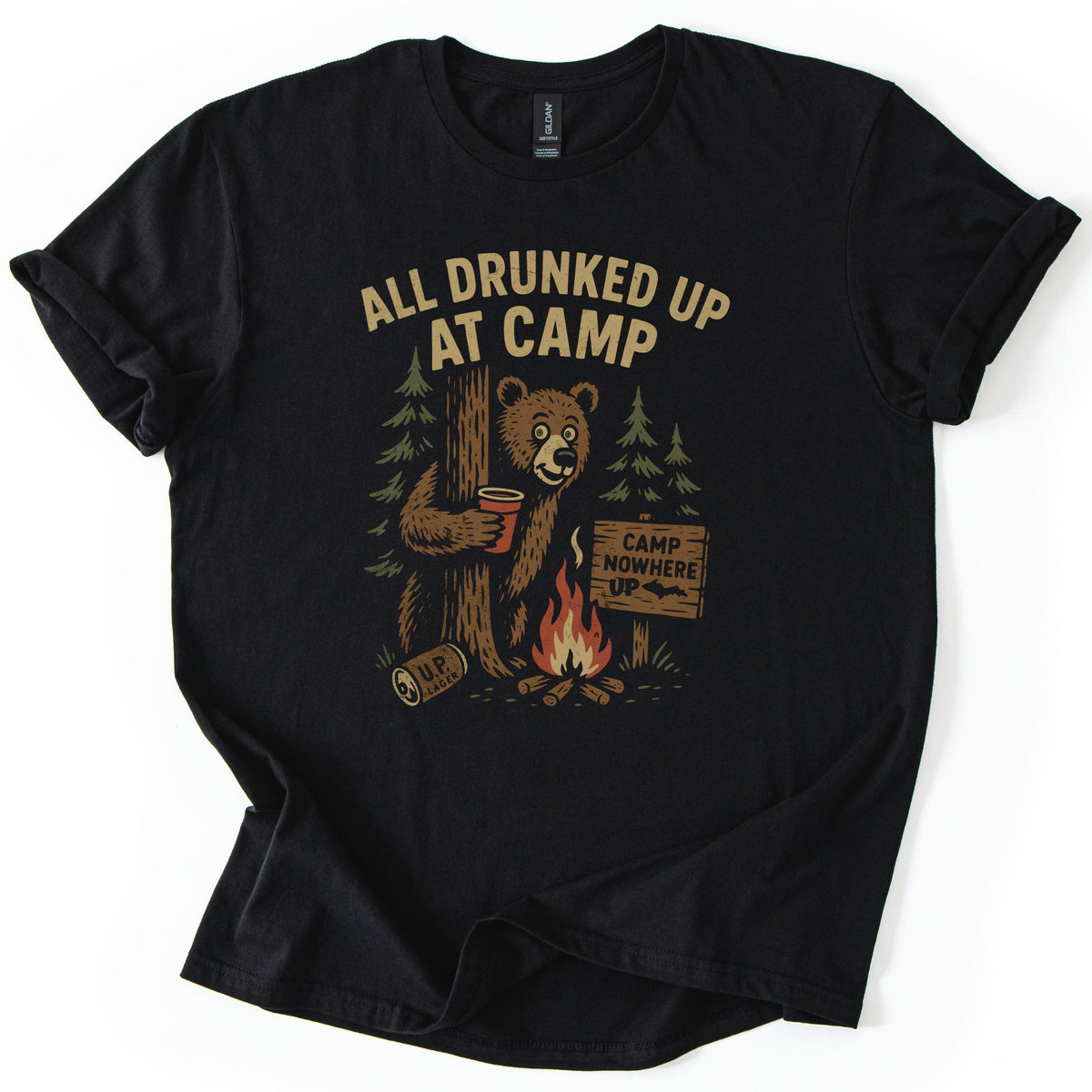 All Drunked Up At Camp Comfort Colors T-shirt in Black, laid flat. A tipsy bear hugs a tree holding a red cup beside a campfire, a fallen UP Lager can, pine trees and a Camp Nowhere UP sign, under the words All Drunked Up At Camp. Sleeves cuffed on a white background.