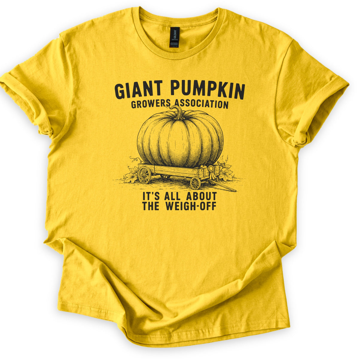 Giant Pumpkin Growers Association Comfort Colors T-shirt in Daisy, laid flat. A black engraving-style drawing of a giant pumpkin on a wooden wagon with a prize ribbon sits between the words Giant Pumpkin Growers Association and It's All About the Weigh-Off. Sleeves cuffed, on white.