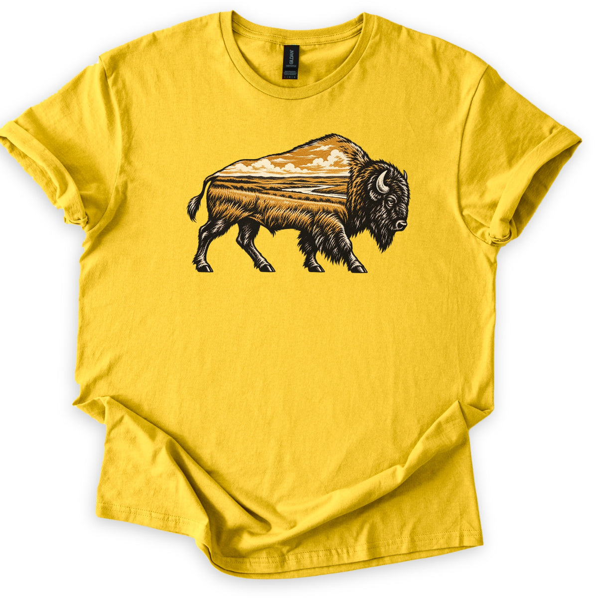 Prairie Bison Comfort Colors T-shirt in Daisy, laid flat. A woodcut-style bison walks in side profile, its body filled with a golden prairie scene of tall grass, a winding river and clouds. No words. The shirt has cuffed sleeves on a white background.