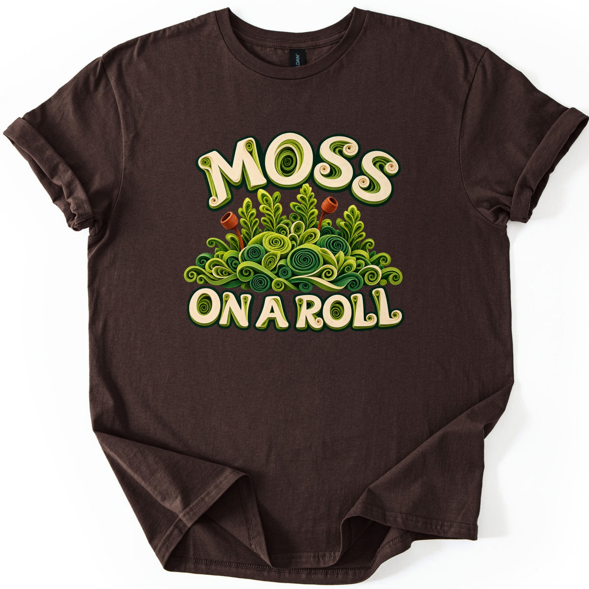 Moss on a Roll Comfort Colors T-shirt in Dark Chocolate, laid flat. Cream lettering reads MOSS above and ON A ROLL below a mound of green paper-quilled moss swirls and fronds with two rust-brown spore capsules. The shirt has cuffed sleeves on a plain white background.
