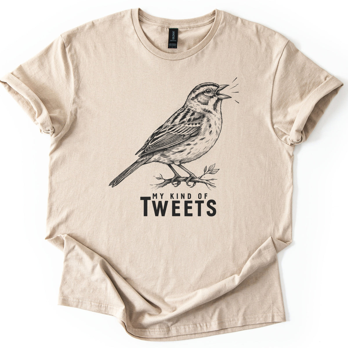 My Kind Of Tweets Comfort Colors T-shirt in Sand, laid flat. A black sketch-style drawing of a sparrow singing on a leafy twig, with short lines by its open beak, above the words My Kind Of Tweets. The sleeves are cuffed and the shirt lies on a white background.