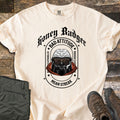 Bad Vibes Badger Comfort Colors T-shirt in Ivory, laid flat. A honey badger in sunglasses and a red hood smokes a cigarette in an arch reading Bad Attitude, Badger Clothing.co, Mean Streak, under Honey Badger in black gothic text. Olive pants and brown boots lie on wood.