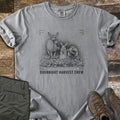 Overnight Harvest Crew Comfort Colors T-shirt in Grey, laid flat. A charcoal sketch of a deer chewing a leaf, a rabbit and a groundhog holding carrots in a cabbage patch, inside camera frame corners above the words Overnight Harvest Crew. Olive pants and brown boots lie on wood.