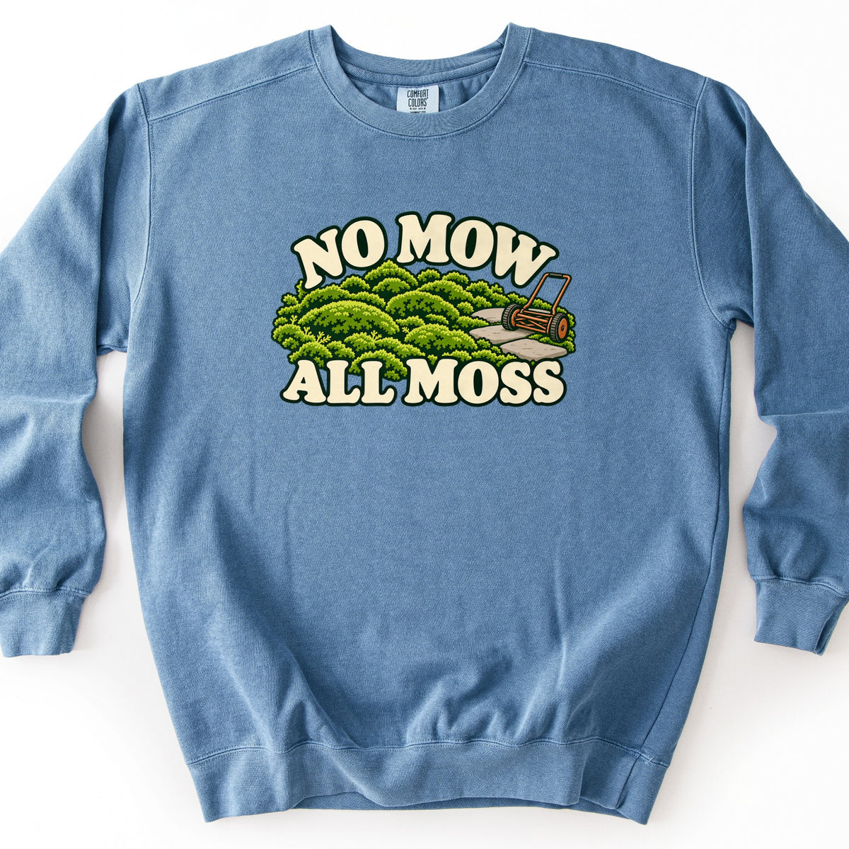 No Mow All Moss Comfort Colors crewneck sweatshirt in Blue Jean, laid flat. Front print shows rounded mounds of green moss with a stone path and an old push reel mower, framed by the words No Mow above and All Moss below in cream lettering. Shown on a plain white background.