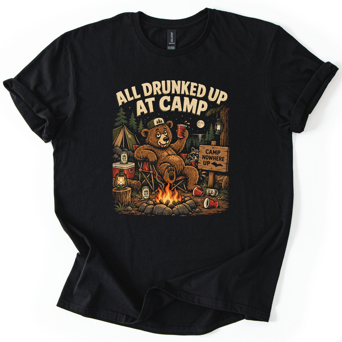 Drunked Up II Comfort Colors T-shirt in Black, laid flat. A bear in a trucker cap lounges in a camp chair by a campfire holding a red cup, under the words All Drunked Up At Camp, with a raccoon, U.P. Lager cans and a Camp Nowhere Up sign. Sleeves rolled, on white.