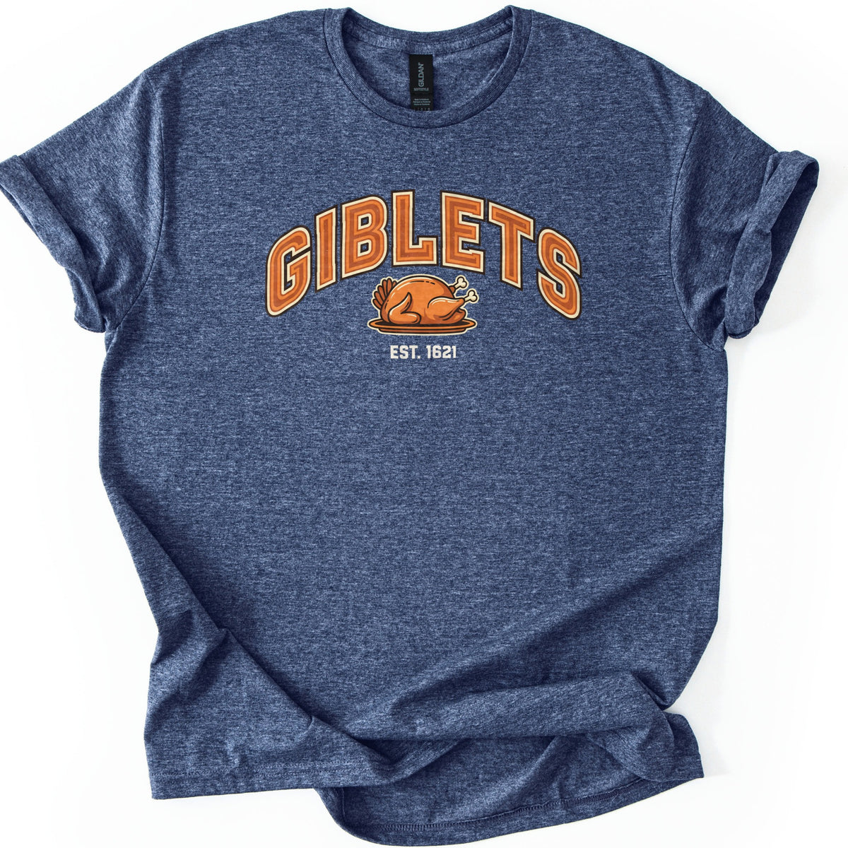 Giblets Comfort Colors T-shirt in Heather Navy, laid flat. Arched orange varsity-style letters read GIBLETS above a cartoon roast turkey on a platter, with EST. 1621 in white below. The shirt has rolled sleeves and lies on a white background.