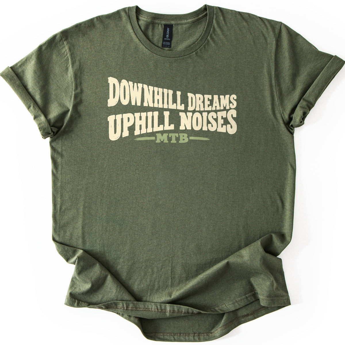 Downhill Dreams Uphill Noises Comfort Colors T-shirt in Military Green, laid flat. Cream wavy lettering reads Downhill Dreams Uphill Noises, with MTB in sage green between two green lines below. The shirt has rolled sleeves and lies on a white background.