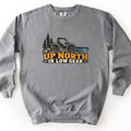 Up North in Low Gear Comfort Colors crewneck sweatshirt in Grey, laid flat. A black and cream side-by-side off-road vehicle sits on rocks between pine trees and a teal lake above the words UP NORTH IN LOW GEAR in gold and cream. It lies on a white background.