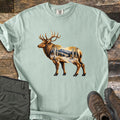 Aspen Pass Elk Comfort Colors T-shirt in Bay, laid flat. A bull elk in profile, its body filled with a snowy mountain scene of aspen trees and pines in golden light. Sleeves rolled, on weathered wood with folded olive hiking pants and brown hiking boots.
