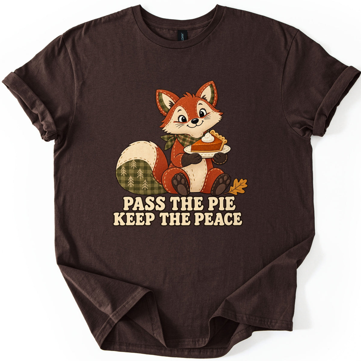 Pass the Pie Keep the Peace Comfort Colors T-shirt in Dark Chocolate, laid flat. A stitched patchwork fox with a green plaid tail and bandana holds a plate of pumpkin pie beside an oak leaf, above the words Pass the Pie Keep the Peace. The sleeves are rolled on a white background.