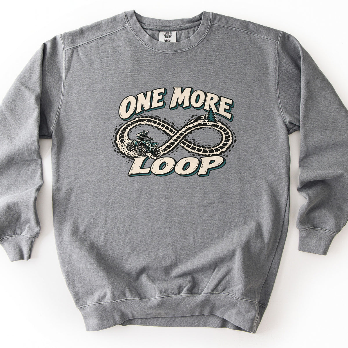 One More Loop Comfort Colors crewneck sweatshirt in Grey, laid flat. The words One More Loop in cream lettering with dark teal shadows surround an infinity-shaped dirt tire track, with a rider on an ATV and a pine tree. Laid flat on a white background.