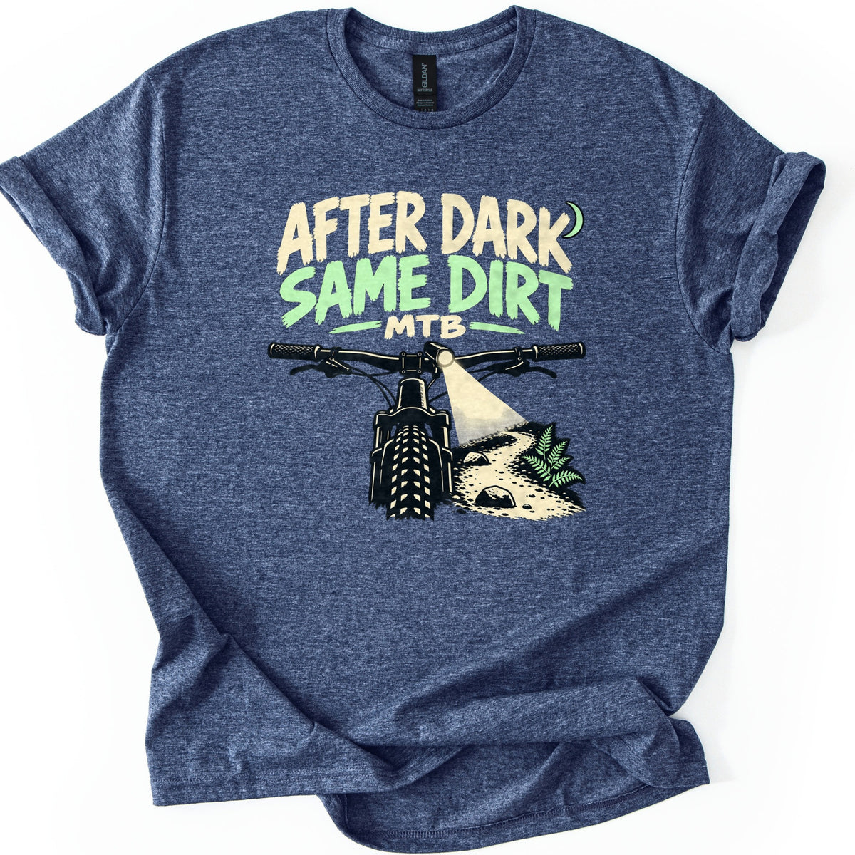 After Dark Same Dirt Comfort Colors T-shirt in Heather Navy, laid flat. A rider's-eye view of mountain bike handlebars, a headlight shining on a rocky dirt trail with a fern, under the words After Dark Same Dirt MTB and a crescent moon. Sleeves rolled, on a white background.