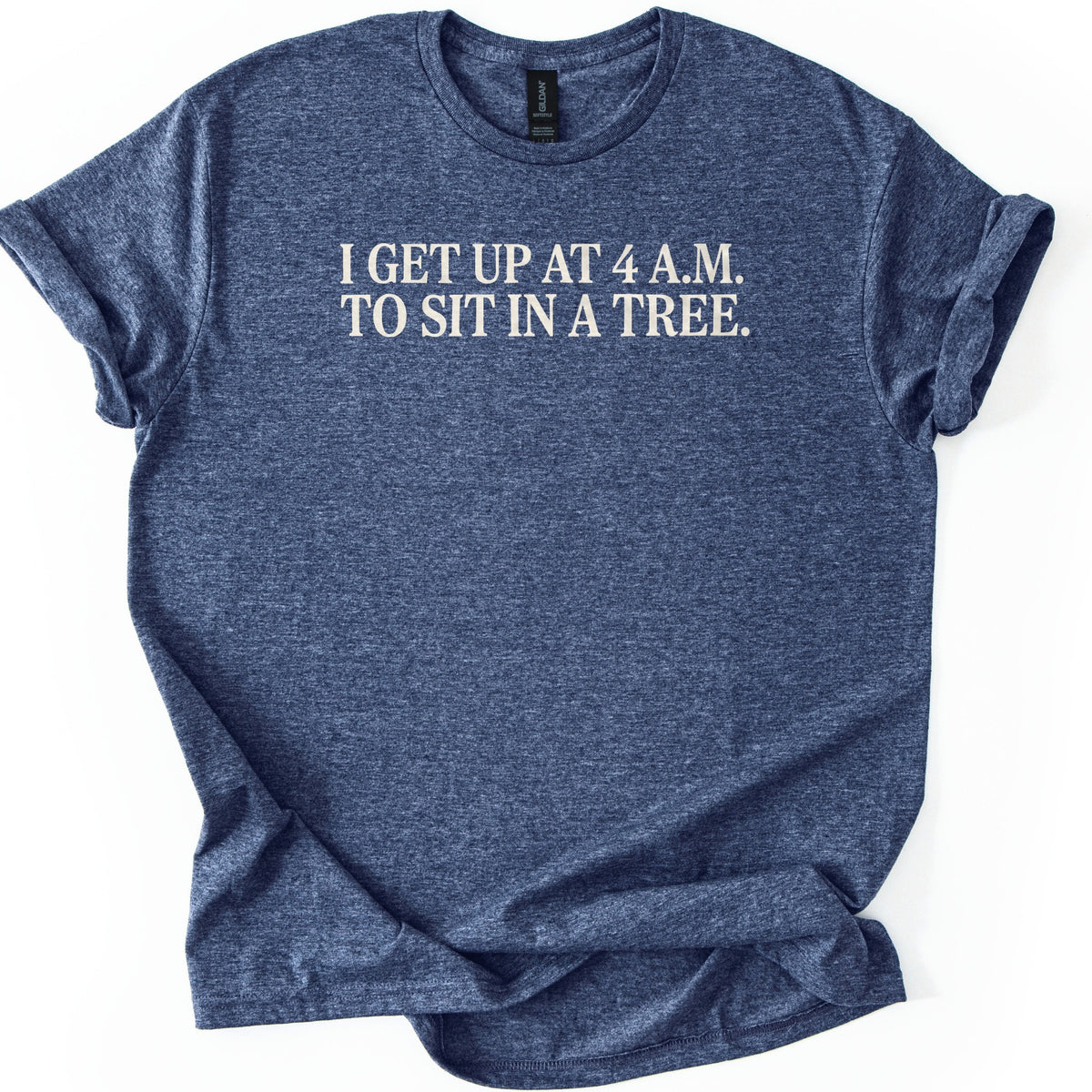 Sit In A Tree Comfort Colors T-shirt in Heather Navy, laid flat. Cream serif capital letters across the chest read I GET UP AT 4 A.M. TO SIT IN A TREE. on two lines. The shirt lies on a white surface with its sleeves rolled and the hem loosely bunched.