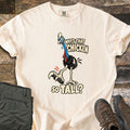 Why's That Chicken So Tall Comfort Colors T-shirt in Ivory, laid flat. A cartoon cassowary with a blue neck, red wattles and a huge clawed foot raised mid-step, with the words Why's That Chicken So Tall? Folded green cargo pants and brown hiking boots sit on weathered wood.
