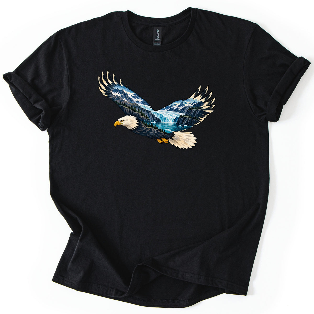 Eagle Glacier Valley Comfort Colors T-shirt in Black, laid flat. A bald eagle in flight, its body and wings filled with a scene of snowy mountains, a glacier, evergreen forest and blue water. No words are printed. The shirt has rolled sleeves on a white background.