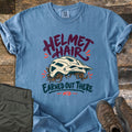 Helmet Hair Earned Out There Comfort Colors T-shirt in Blue Jean, laid flat. A cream mountain bike helmet with curly brown hair poking out below sits between the words Helmet Hair and Earned Out There, with MTB underneath. Folded olive hiking pants and brown boots lie beside it on wood planks.