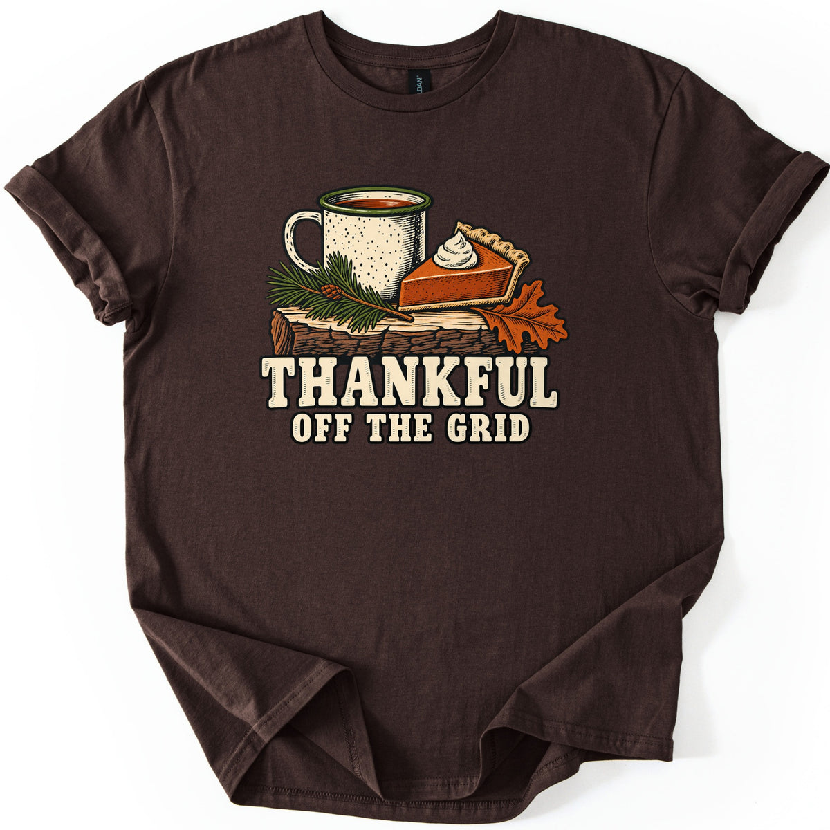 Thankful Off the Grid Comfort Colors T-shirt in Dark Chocolate, laid flat. A speckled enamel camp mug of coffee, a slice of pumpkin pie with whipped cream, a pine sprig and an orange oak leaf sit on a log above the words Thankful Off the Grid. The shirt lies on a plain white background.