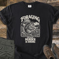 Foraging Murder Squirrel Comfort Colors T-shirt in Black, laid flat. Cream engraving-style art of a squirrel with a backpack holding a mushroom by a basket of mushrooms, forest and mountains behind, reads Foraging, Because Murder Is Wrong. Green pants and brown boots on wood.