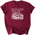 Got Rapids Comfort Colors T-shirt in Maroon, laid flat. White line art shows a man raising a paddle overhead and a smiling woman paddling a raft through splashing whitewater, under the words Got Rapids? The sleeves are rolled on a white background.