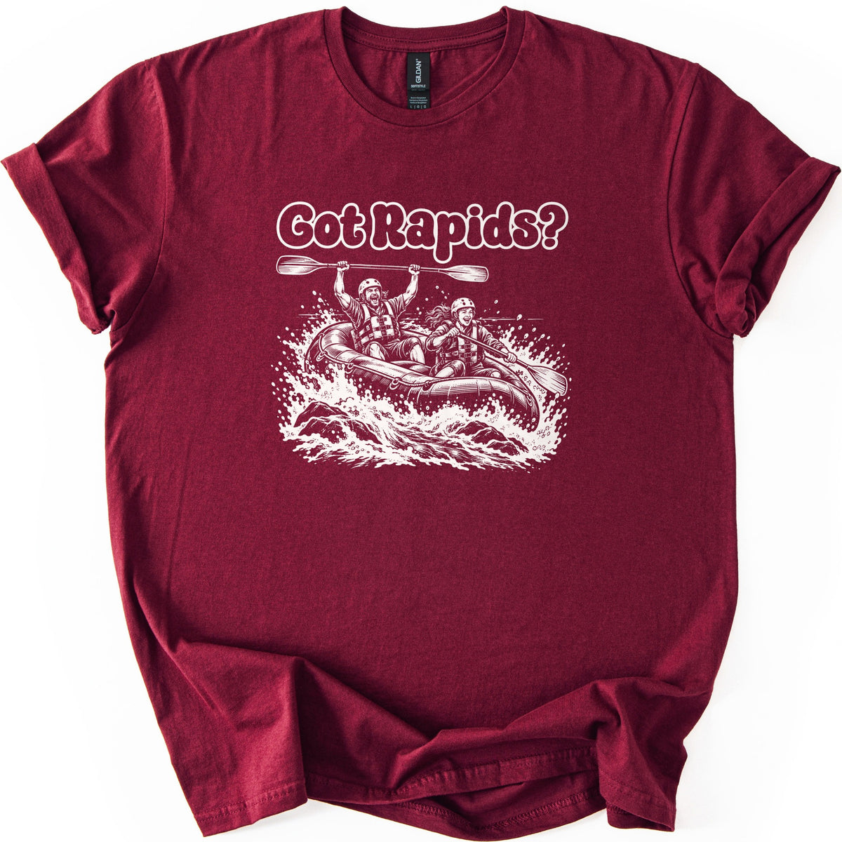 Got Rapids Comfort Colors T-shirt in Maroon, laid flat. White line art shows a man raising a paddle overhead and a smiling woman paddling a raft through splashing whitewater, under the words Got Rapids? The sleeves are rolled on a white background.