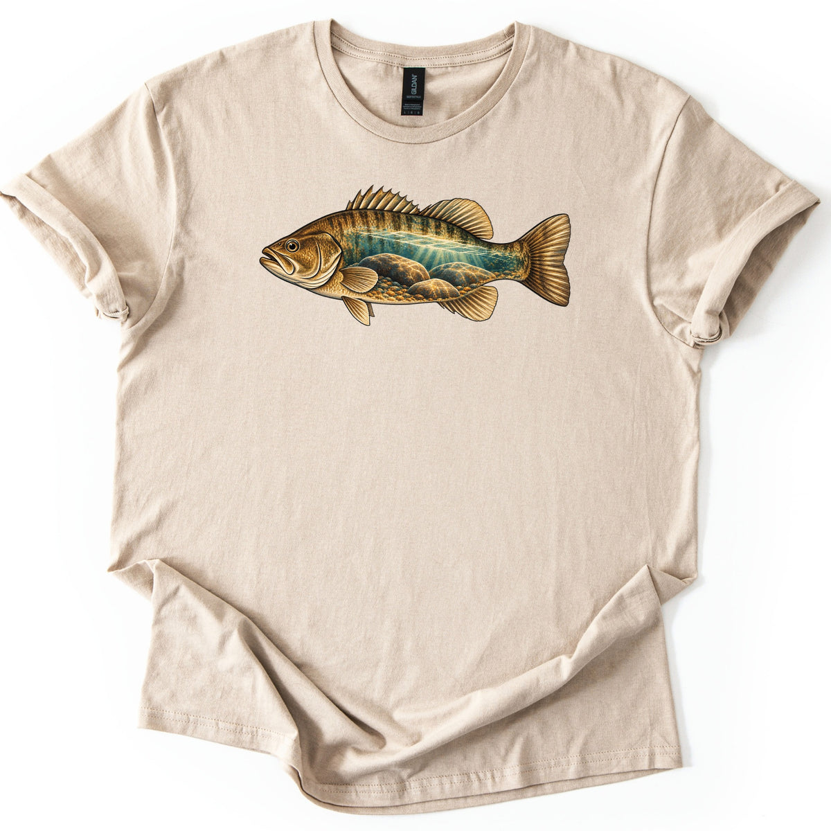 Rocky Shallows Bass Comfort Colors T-shirt in Sand, laid flat. A gold and brown bass is printed across the chest, its body filled with an underwater scene of teal water, light rays and rounded rocks. No words are printed. The shirt has rolled sleeves on a white background.