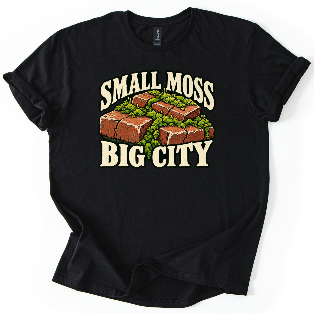 Small Moss Big City Comfort Colors T-shirt in Black, laid flat. A cluster of red bricks overgrown with green moss sits between the words SMALL MOSS and BIG CITY in cream letters. The shirt has rolled sleeves and lies on a white background.