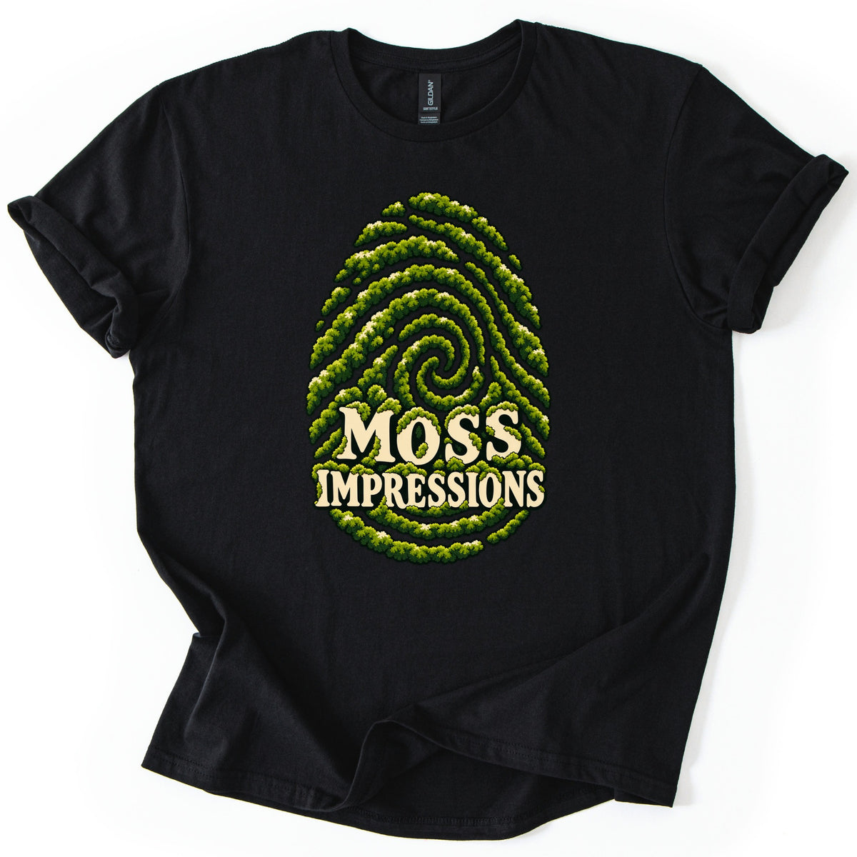 Moss Impressions Comfort Colors T-shirt in Black, laid flat. A large fingerprint formed from swirling green moss ridges, with the words Moss Impressions in cream lettering across its lower half. The shirt has rolled sleeves and lies on a white background.