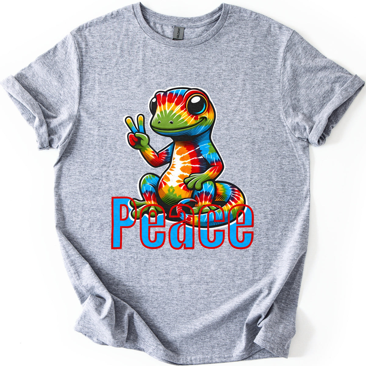 Rainbow Lizard Peace Comfort Colors T-shirt in Sport Grey, laid flat. A smiling cartoon lizard with tie-dye rainbow skin sits on its curled tail and flashes a peace sign above the word Peace in blue letters outlined in red. Cuffed sleeves on a white background.