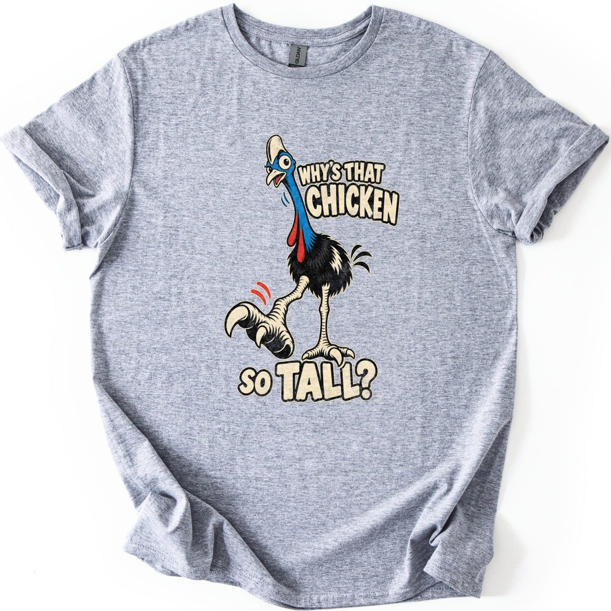 Why's That Chicken So Tall Comfort Colors T-shirt in Sport Grey, laid flat. A wide-eyed cartoon cassowary with a blue head, red wattles and black feathers lifts a huge clawed foot under the words Why's That Chicken So Tall? The shirt lies on a white surface with cuffed sleeves.