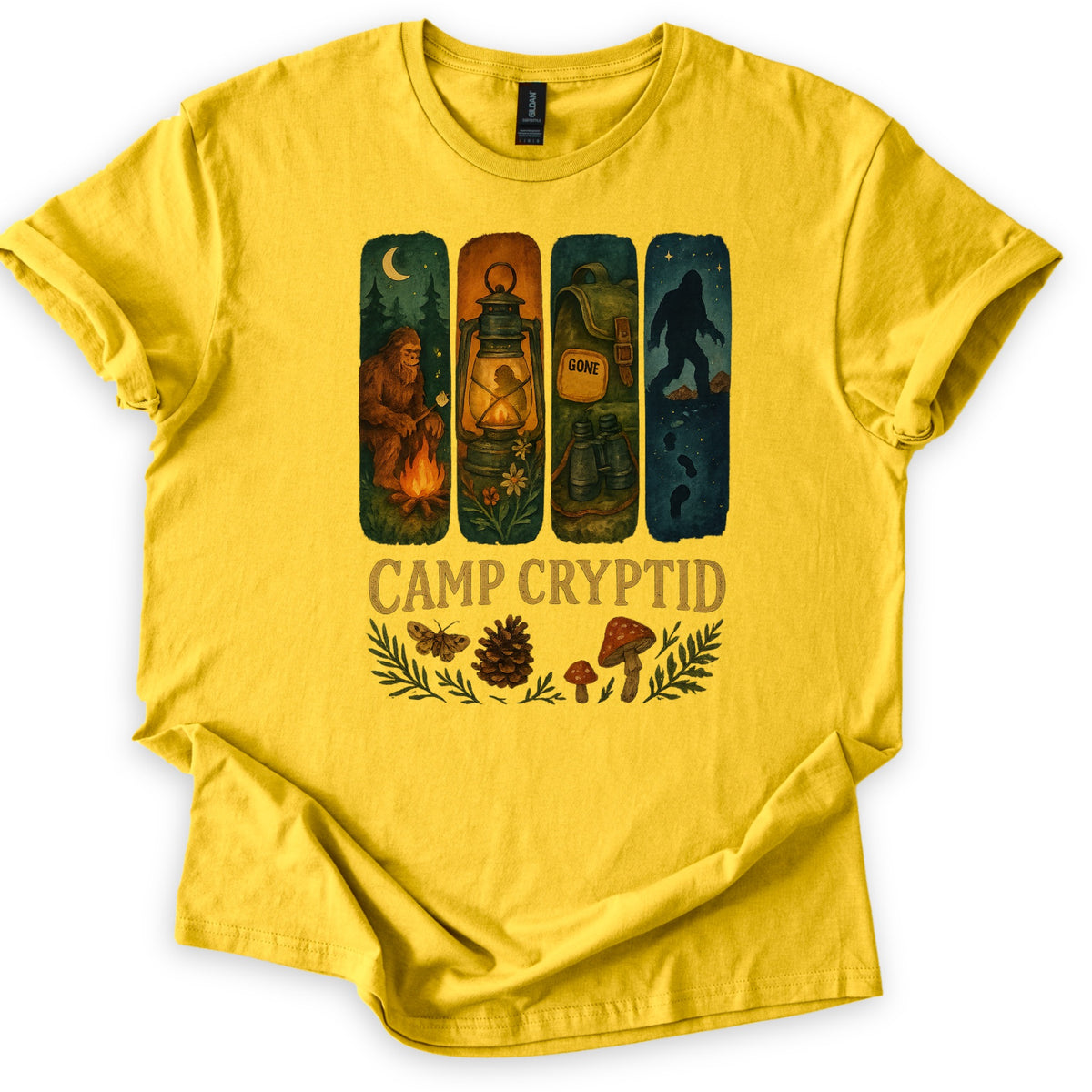 Camp Cryptid Big Foot Comfort Colors T-shirt in Daisy, laid flat. Four painted panels show Bigfoot at a campfire, a lit lantern, a backpack marked GONE, and Bigfoot's silhouette under stars, above the words Camp Cryptid and a moth, pinecone and mushrooms. Shown on a white background.