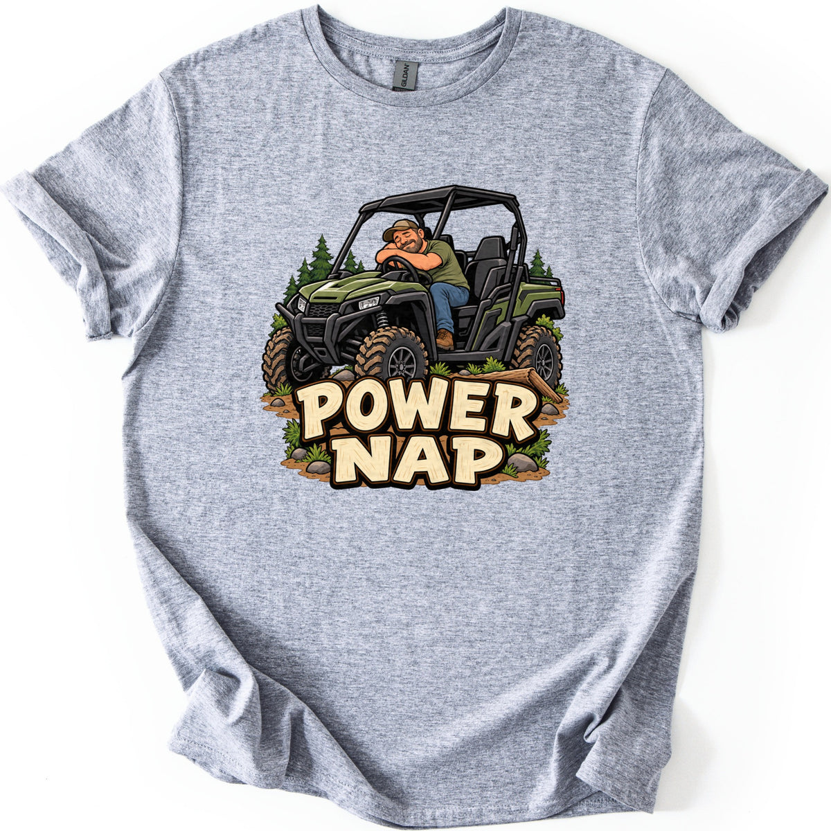 Power Nap Comfort Colors T-shirt in Sport Grey, laid flat. A cartoon man in a cap and jeans naps over the steering wheel of a green side-by-side UTV on a dirt trail with pines, above the words Power Nap. The shirt lies flat on a white background.