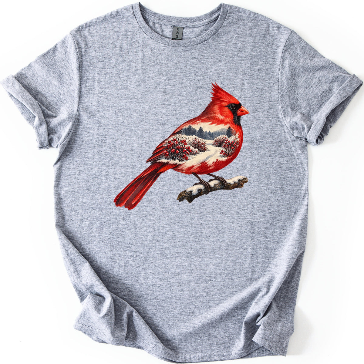 Winter Cardinal Comfort Colors T-shirt in Sport Grey, laid flat. A painted red cardinal perches on a snowy branch, its body filled with a winter scene of evergreens, a snowy path and red-berry bushes. No words are printed. The sleeves are cuffed on a white background.