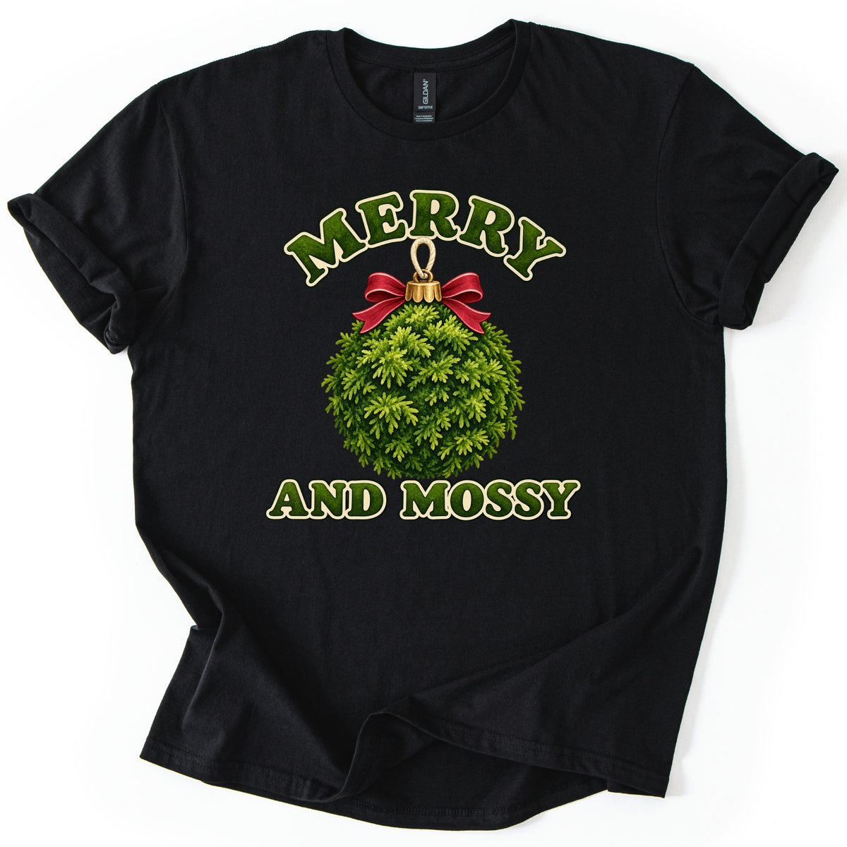 Merry and Mossy Comfort Colors T-shirt in Black, laid flat. A round ornament made of green moss with a red bow and gold cap sits between the words Merry and Mossy in green moss-textured letters outlined in cream. Sleeves are rolled on a white background.