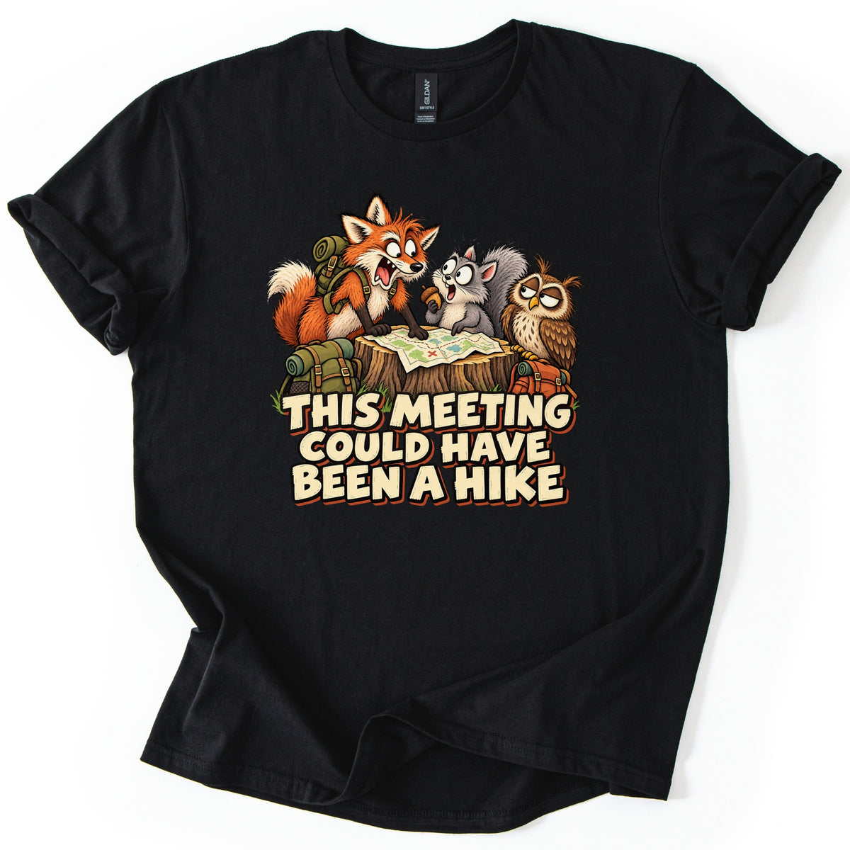 This Meeting Could Have Been a Hike Comfort Colors T-shirt in Black, laid flat. A startled cartoon fox points at a trail map on a tree stump beside a squirrel and a sleepy owl, above the words This Meeting Could Have Been a Hike. The shirt lies on a white background.