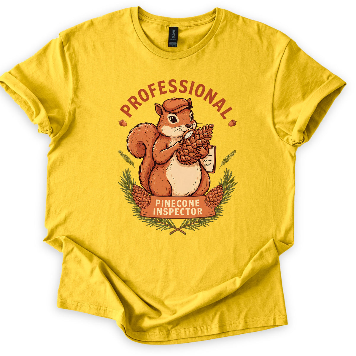 Professional Pinecone Inspector Comfort Colors T-shirt in Daisy, laid flat. A squirrel in a cap inspects a pinecone with a magnifying glass under the arched word Professional in rust red, above a banner reading Pinecone Inspector framed by pine branches. Sleeves are cuffed on a white surface.