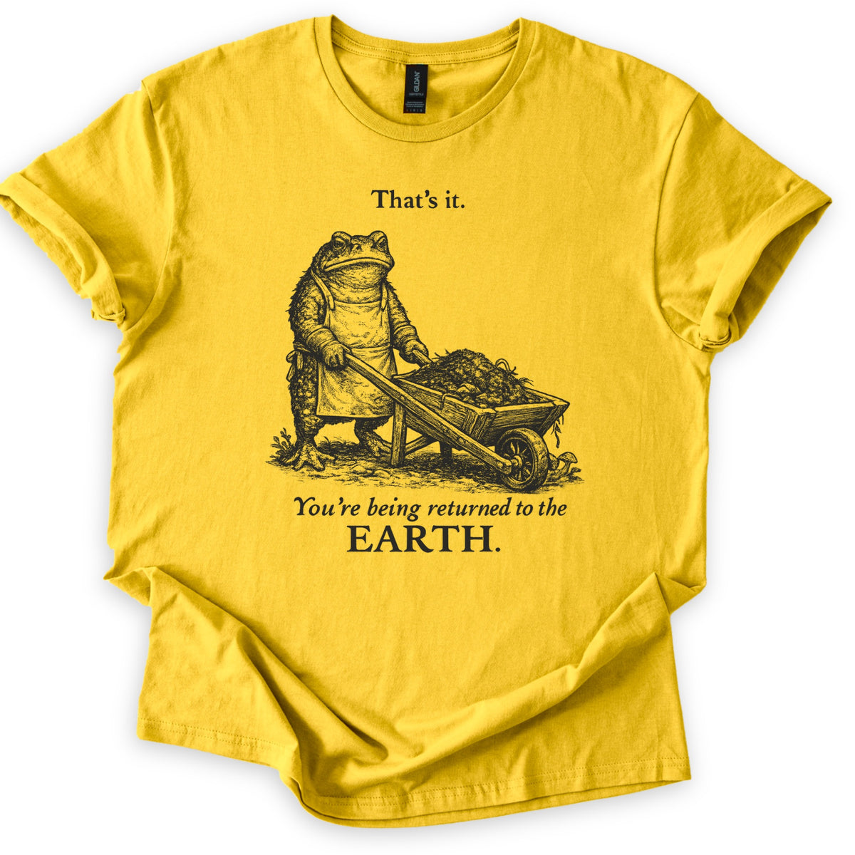 Toad Compost Comfort Colors T-shirt in Daisy, laid flat. A black ink etching of a frowning toad in an apron pushing a wheelbarrow of compost, between the words That's it. and You're being returned to the EARTH. Sleeves are cuffed on a white background.